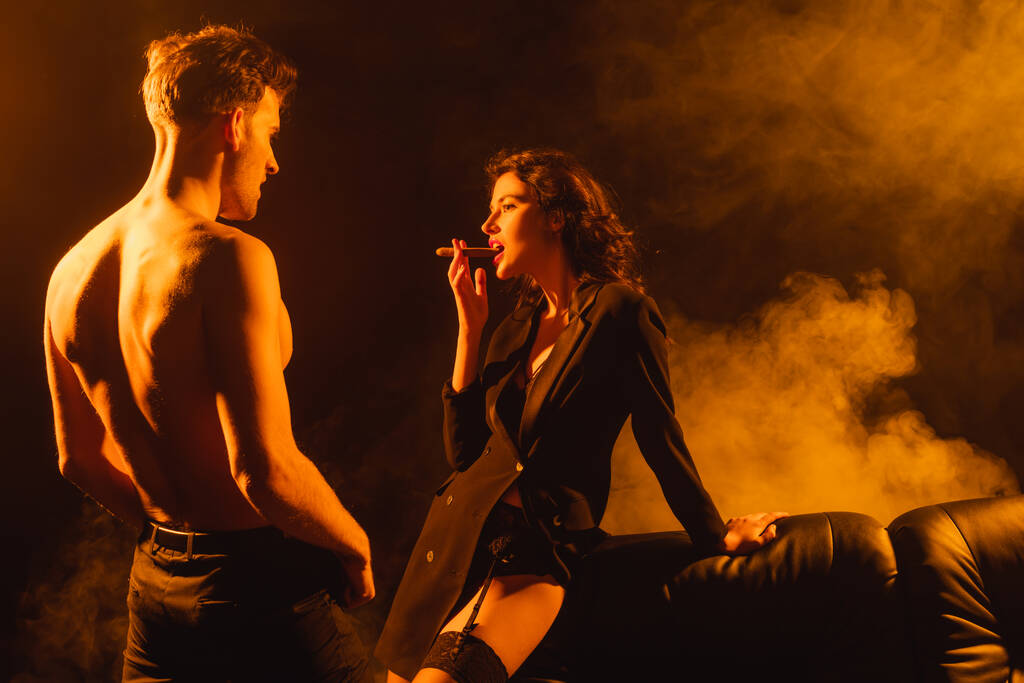 donna seducente fumare sigaro vicino a camicia uomo su nero - Foto, immagini