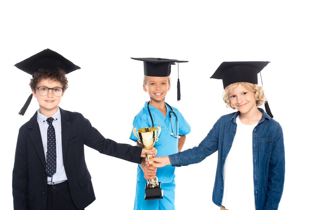 children in graduation caps dressed in costumes of different professions holding golden trophy isolated on white  - Photo, Image