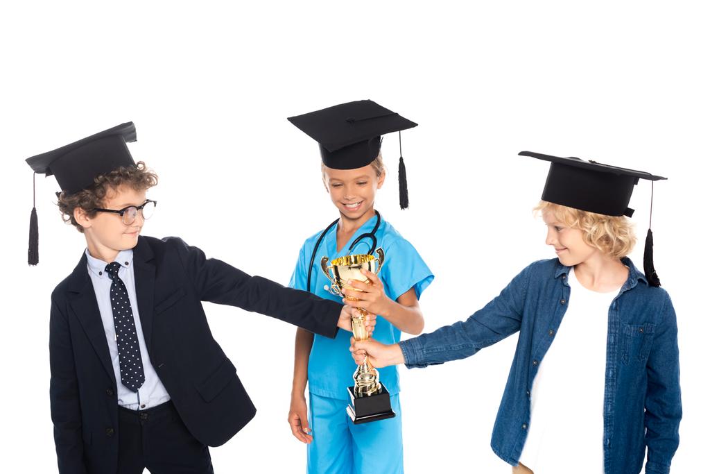 niños con gorras de graduación vestidos con disfraces de diferentes profesiones sosteniendo trofeo dorado aislado en blanco  - Foto, imagen