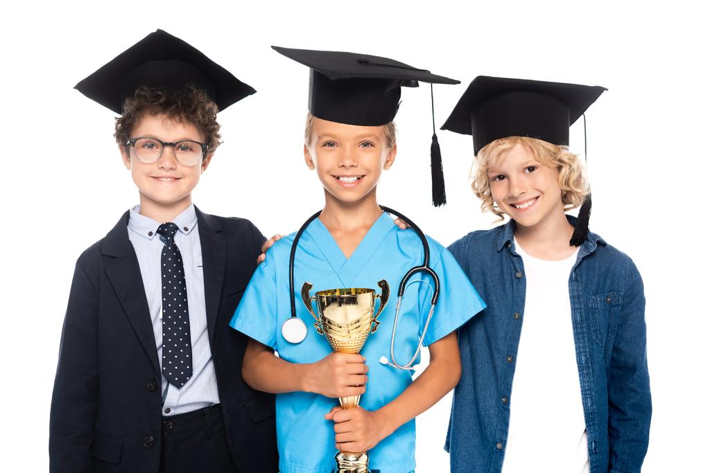 dzieci w czapkach dyplomowych ubrane w kostiumy różnych zawodów posiadających trofeum izolowane na białym  - Zdjęcie, obraz