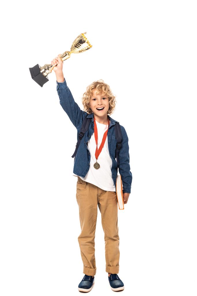 krullenbol schooljongen met gouden medaille houden trofee en boek geïsoleerd op wit  - Foto, afbeelding