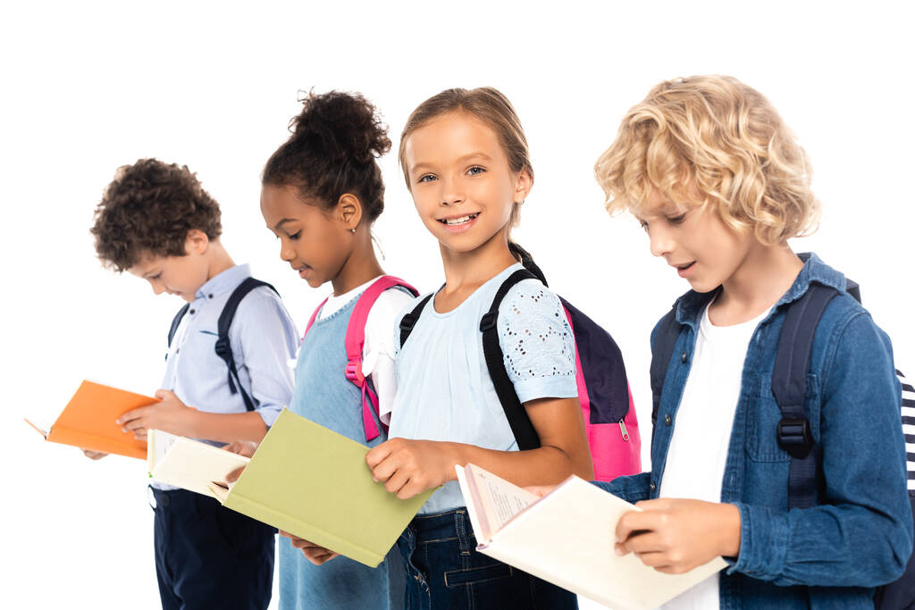 селективное внимание мультикультурных школьников с рюкзаками с книгами, изолированными на белом  - Фото, изображение