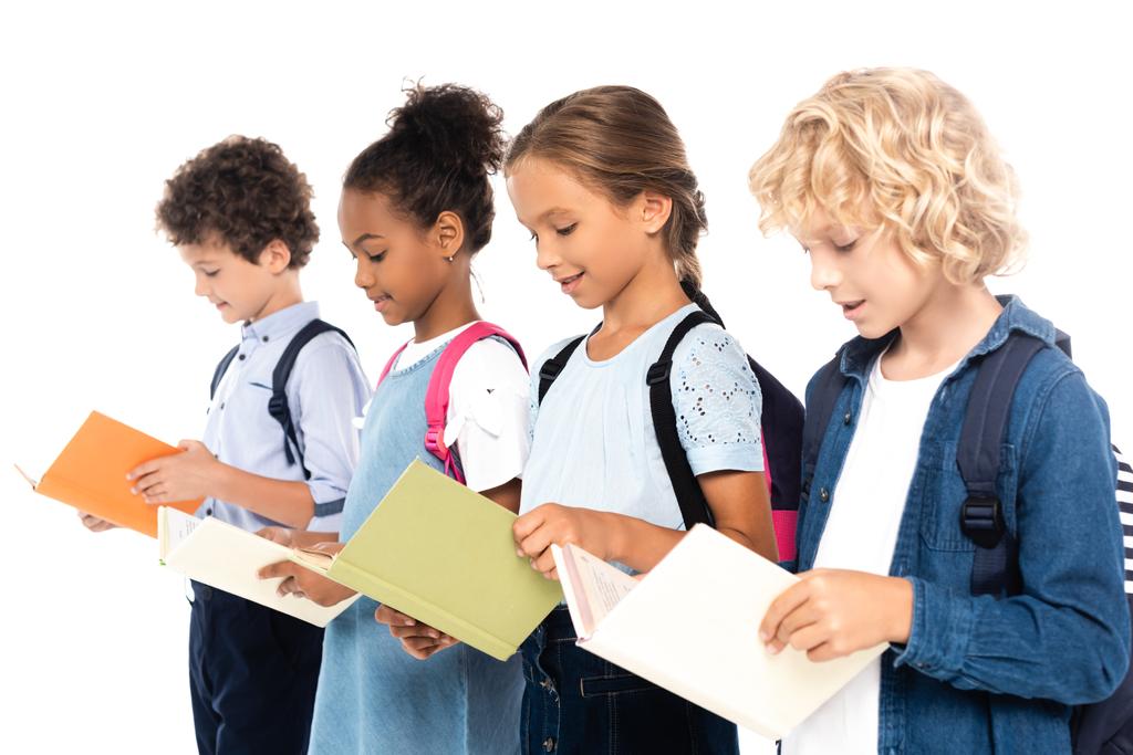 selectieve focus van multiculturele schoolkinderen met rugzakken leesboeken geïsoleerd op wit  - Foto, afbeelding