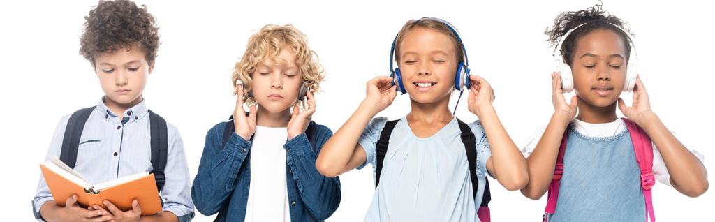 panoramica di scolari multiculturali ascoltare musica in cuffie wireless vicino ricci ragazzo lettura libro isolato su bianco  - Foto, immagini