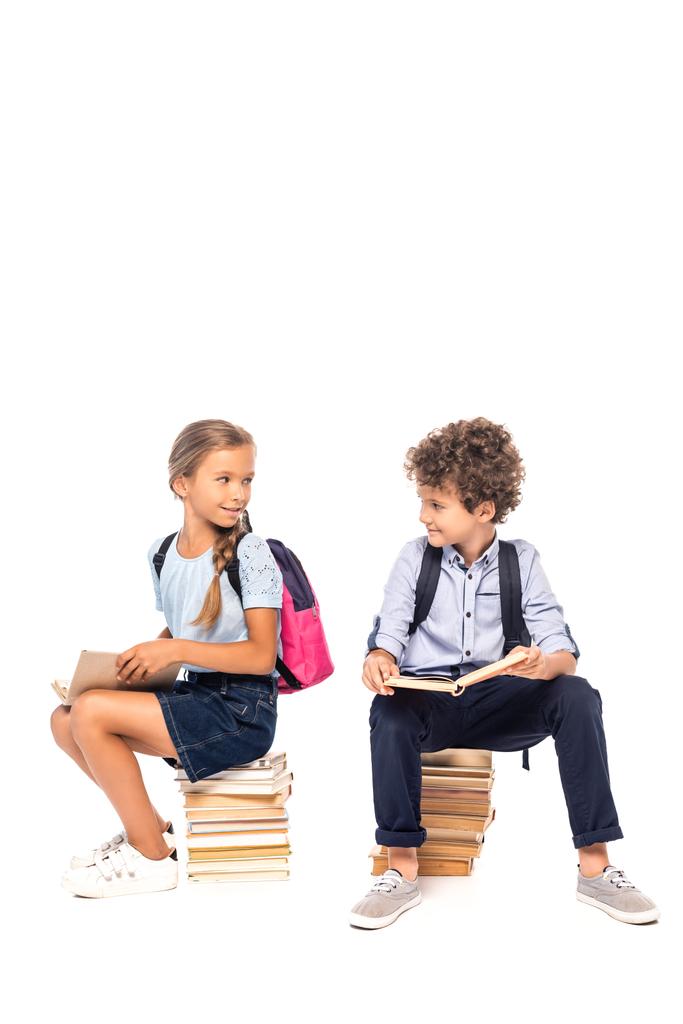 schoolkids sitting on books and looking at each other isolated on white - Photo, Image