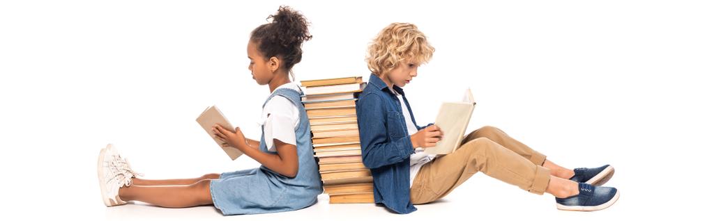 panoramisches Konzept multikultureller Kinder, die in der Nähe von Büchern sitzen und isoliert auf weißem Papier lesen  - Foto, Bild