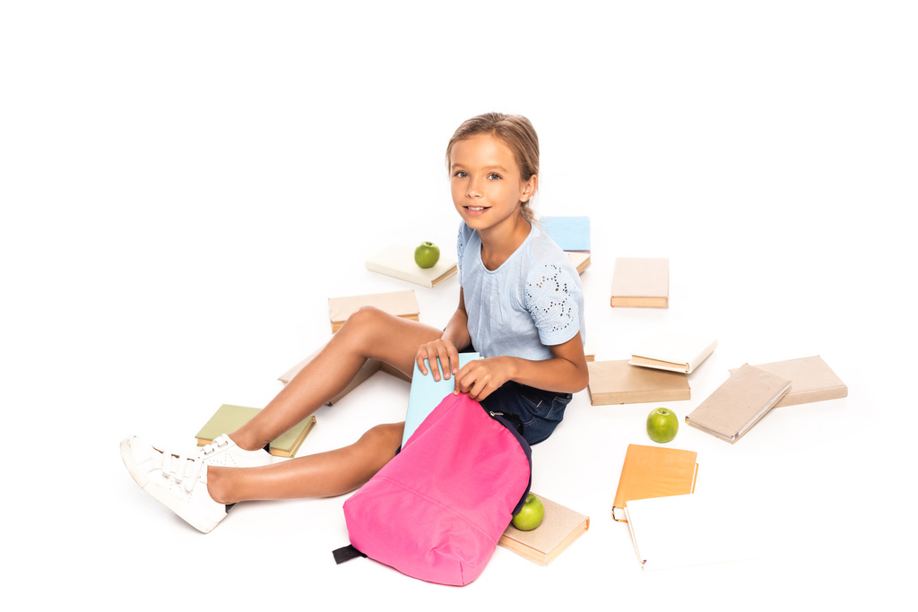 Liseli kız elmaların yanında oturuyor ve kitabı beyaz bir çantaya koyuyor. - Fotoğraf, Görsel