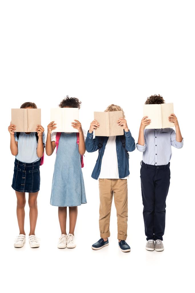 wielokulturowe dzieci szkolne przykrywające twarze książkami odizolowanymi na białym  - Zdjęcie, obraz