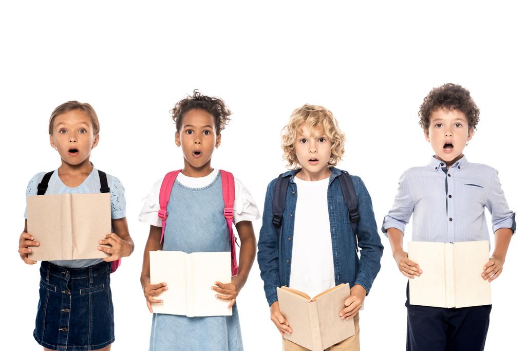šokované multikulturní školačky a školáci držící knihy izolované na bílém  - Fotografie, Obrázek