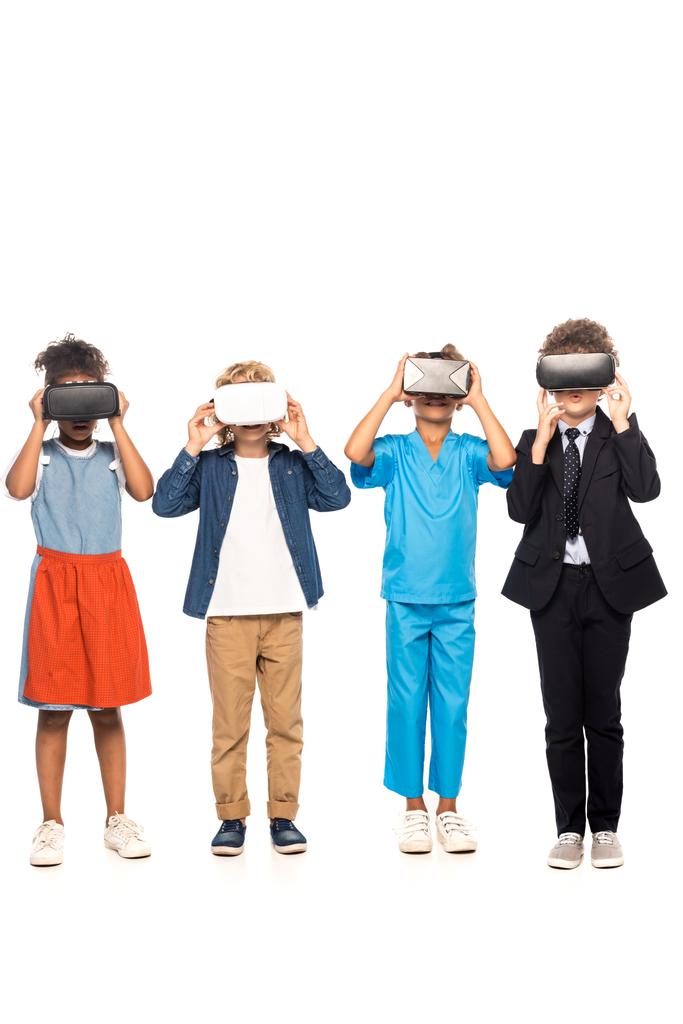 multiculturele kinderen gekleed in kostuums van verschillende beroepen raken virtuele realiteit headsets geïsoleerd op wit  - Foto, afbeelding