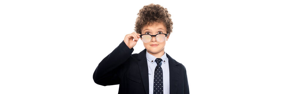 panoramisch gewas van krullende jongen in pak aanraken bril en kijken naar camera geïsoleerd op wit - Foto, afbeelding