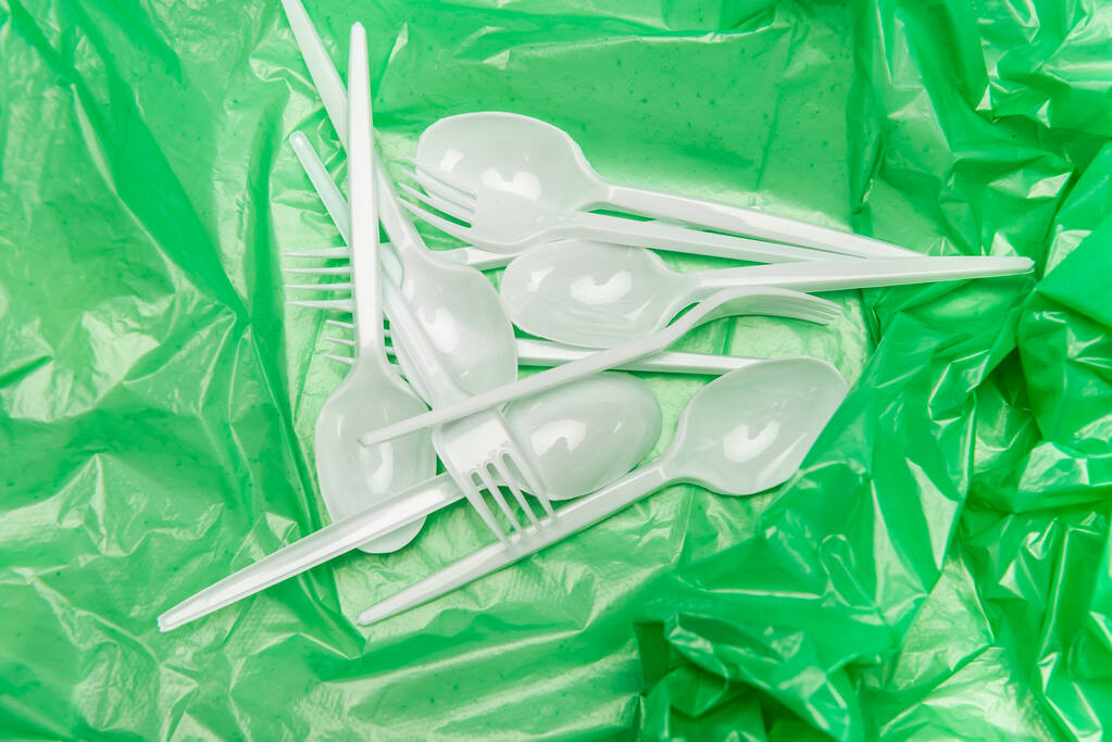 vista dall'alto di posate monouso bianche su texture plastica verde - Foto, immagini