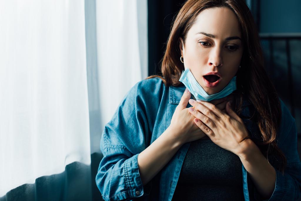 喉に触れる医療用マスクの開いた口を持つ恐怖の女性  - 写真・画像