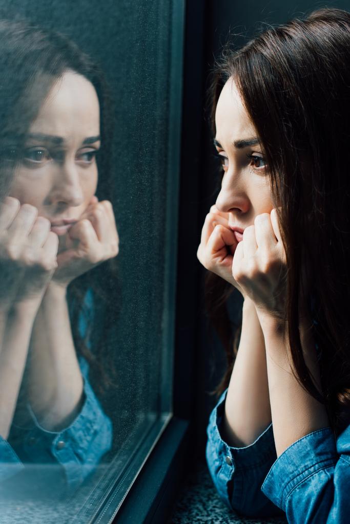 triste bruna donna toccare il viso mentre guardando la finestra  - Foto, immagini