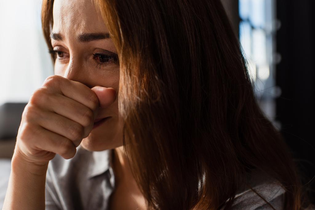 primer plano de mujer molesta y morena tocando la cara mientras llora en casa - Foto, Imagen