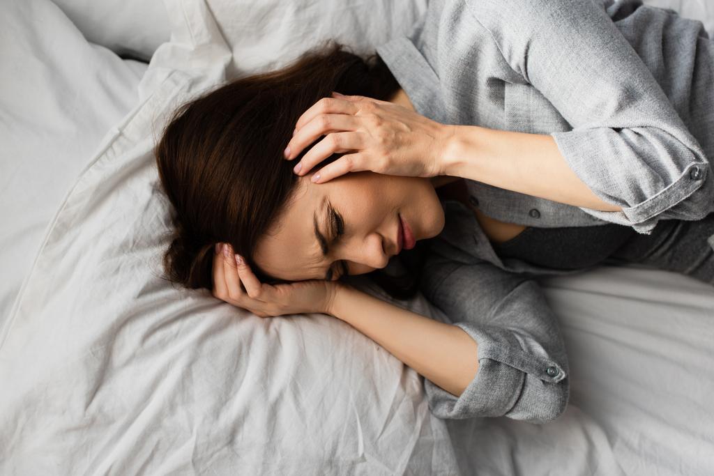 vista dall'alto di donna stanca con emicrania, testa toccante e sdraiata sul letto - Foto, immagini