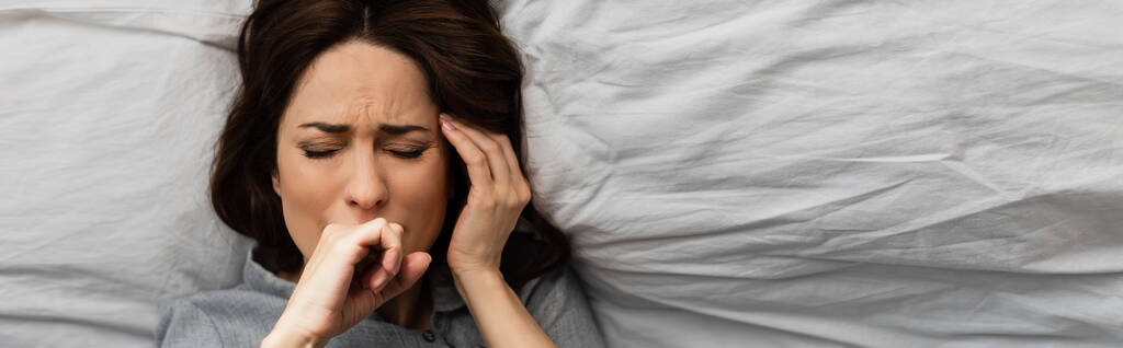 horizontální plodiny bruneta žena trpí bolestí a dotekem hlavy při ležení na posteli  - Fotografie, Obrázek