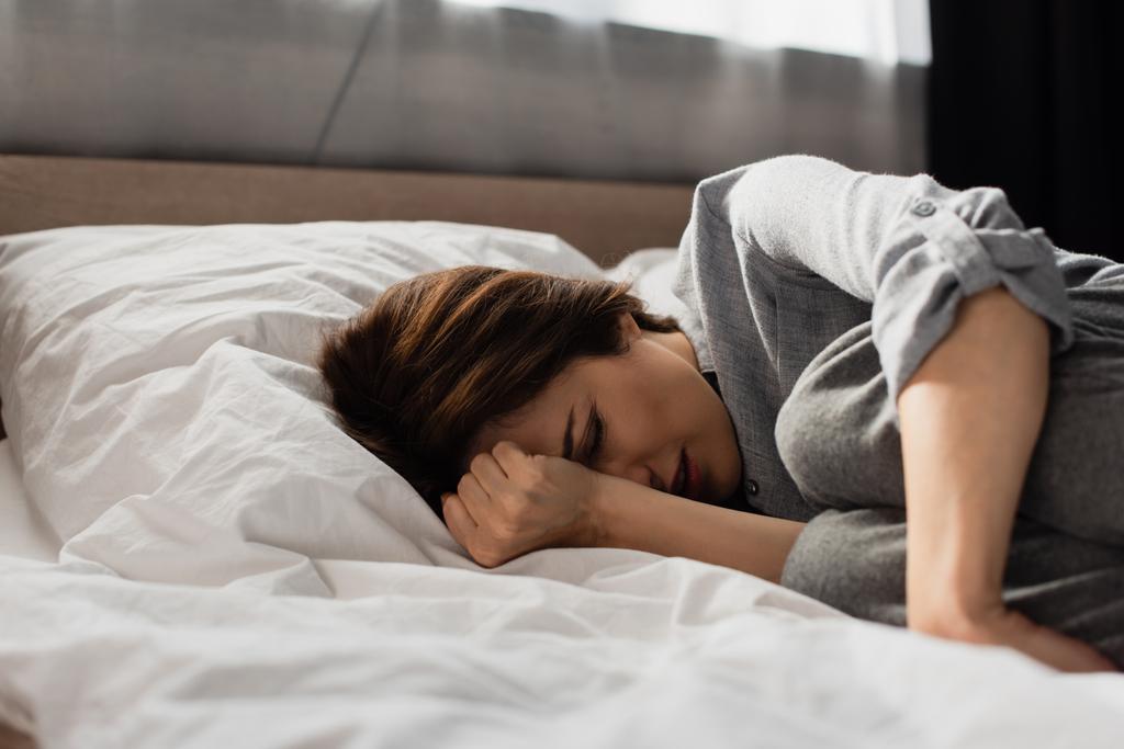 wyczerpana kobieta cierpiąca na ból i dotykająca głowy leżąca na łóżku  - Zdjęcie, obraz