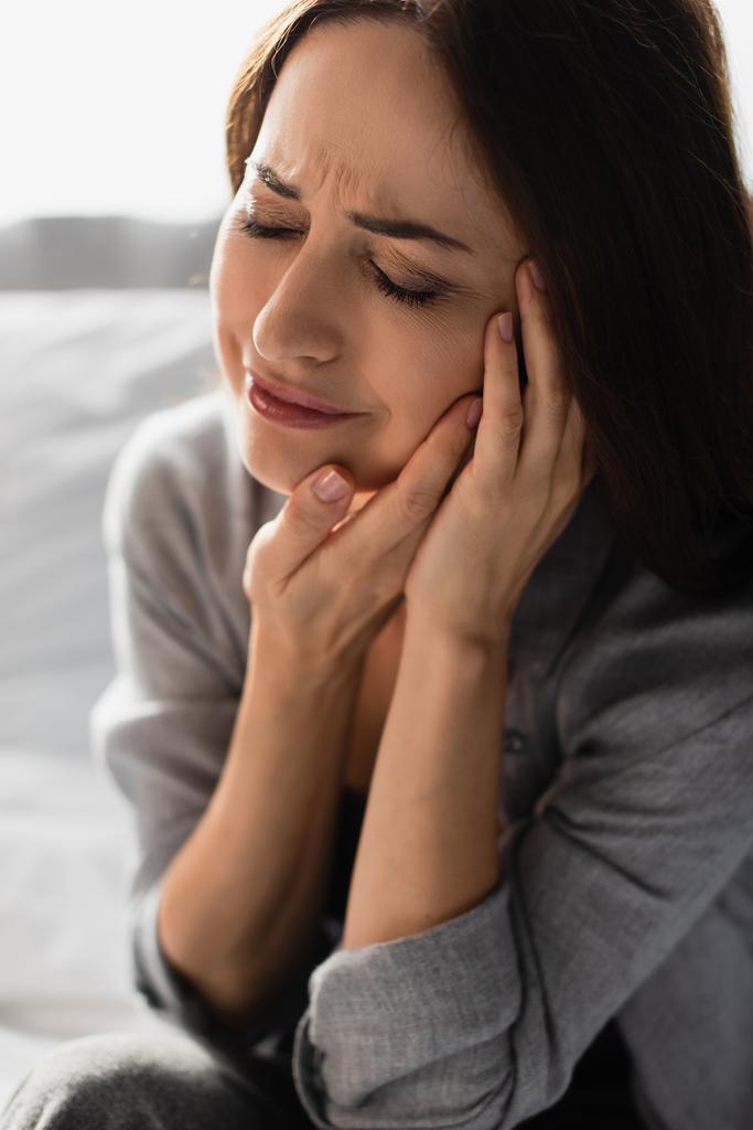 femme brune avec les yeux fermés touchant le visage tout en souffrant de maux de dents à la maison - Photo, image