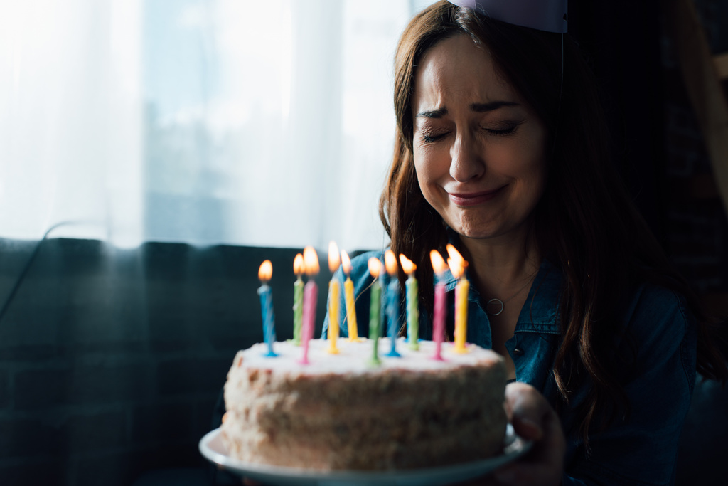 selectieve focus van trieste vrouw huilen terwijl het houden van verjaardagstaart met kaarsen  - Foto, afbeelding