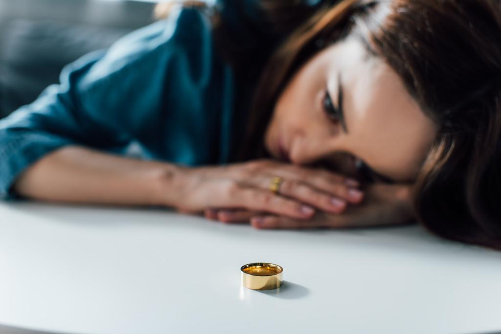 Selektiver Fokus depressiver Frau auf Couchtisch mit goldenem Ring, Scheidungskonzept  - Foto, Bild
