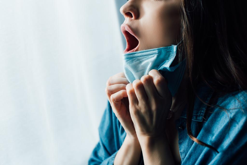 částečný pohled vyděšené ženy s otevřenými ústy dotýkající se lékařské masky  - Fotografie, Obrázek