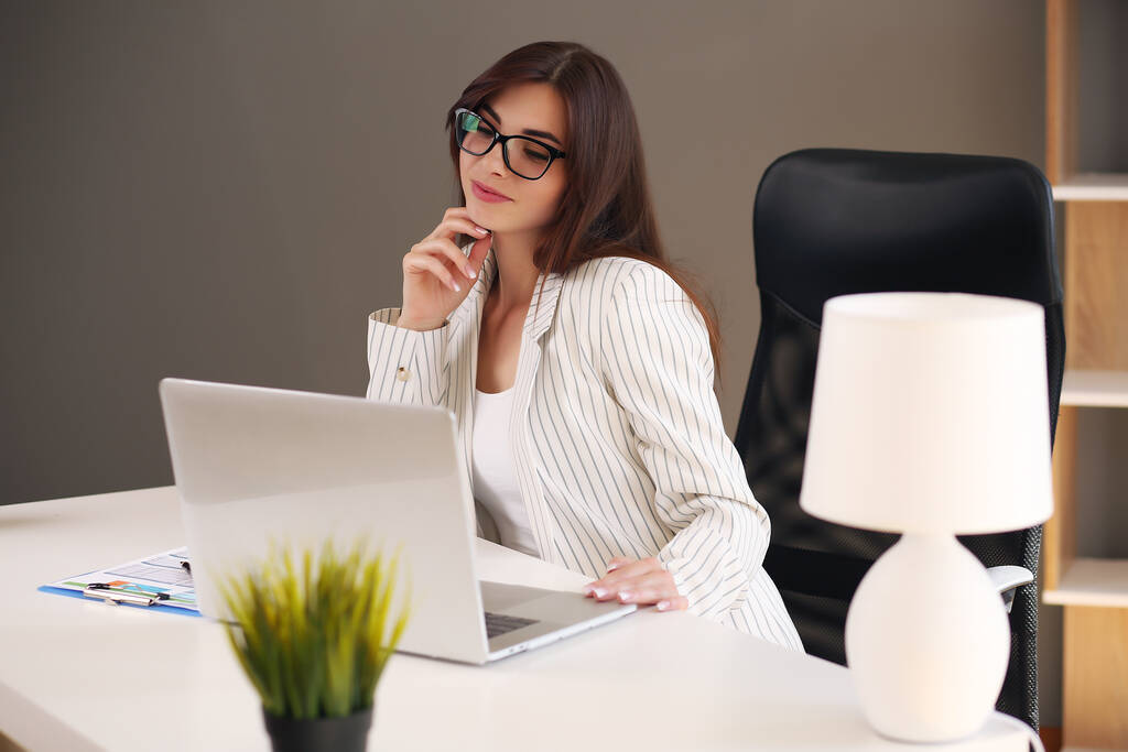 Bella donna d'affari utilizza un computer portatile e sorride mentre lavora in ufficio - Foto, immagini