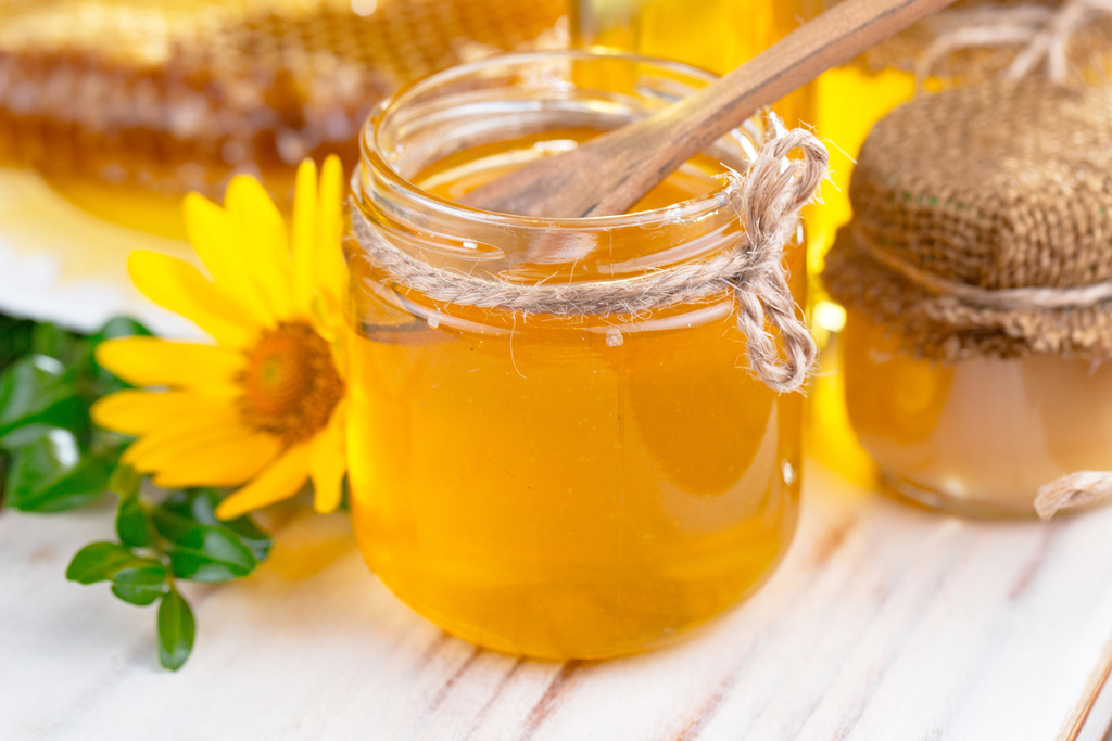 Бджолиний мед в банці з квіткою, на старому тлі
. - Фото, зображення