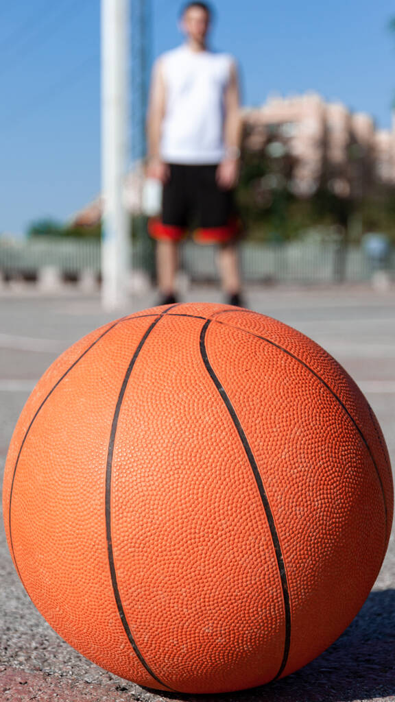Vertikální selektivní zaostření záběru basketbalového míče u soudu a osoby v pozadí - Fotografie, Obrázek