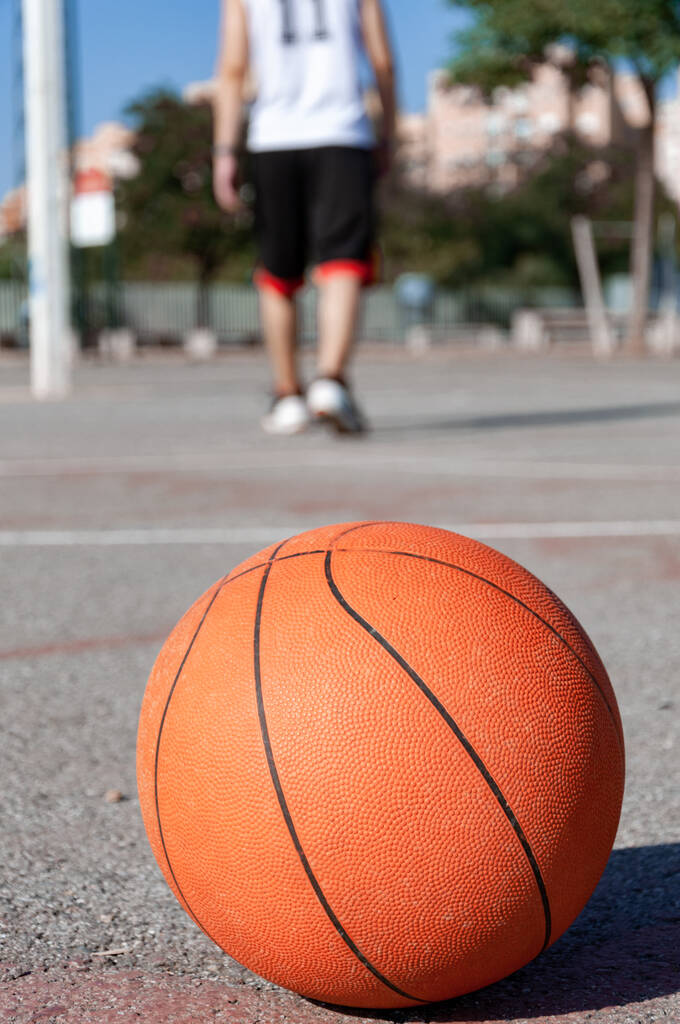 Un tiro de enfoque selectivo vertical de una pelota de baloncesto en una cancha y una persona en el fondo - Foto, Imagen