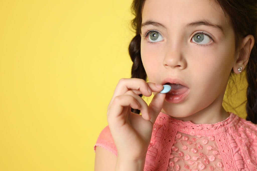 Little girl taking vitamin pill on yellow background, closeup. Space for text - Photo, Image
