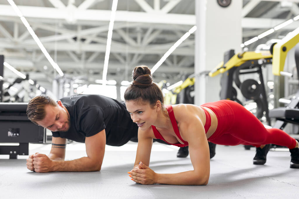 joven hombre y mujer de pie en posición de tablón en el gimnasio - Foto, imagen