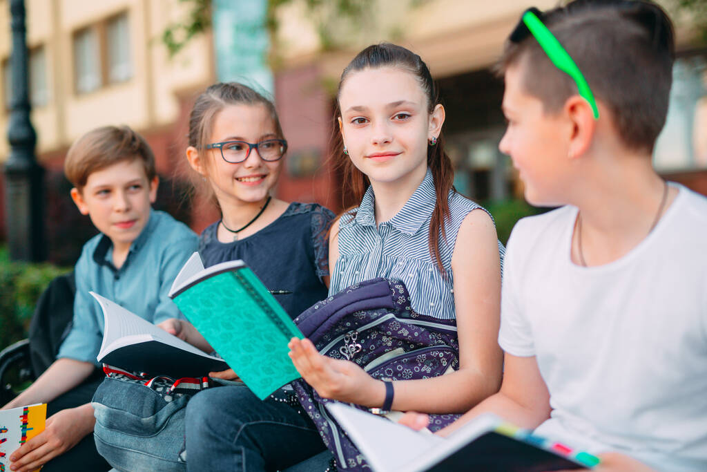 Glückliche Schulkameraden. Mitschüler sitzen mit Büchern auf einer Holzbank im Stadtpark und lernen an sonnigen Tagen. - Foto, Bild