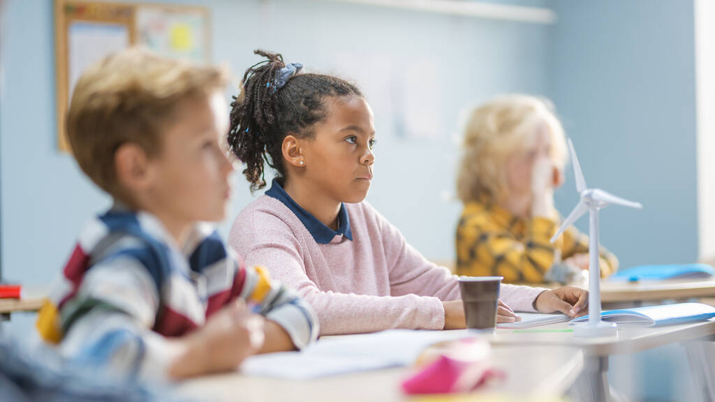 In de basisschool klaslokaal Briljant zwart meisje is zorgvuldig luisteren naar een leraar. Junior klaslokaal met groep van heldere kinderen die ijverig werken en nieuwe dingen leren - Foto, afbeelding