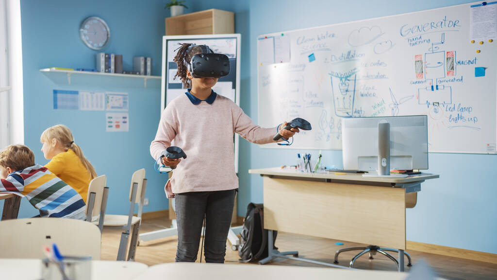 Elementary School Computer Science Class: Cute Girl Wearing Augmented Reality Headset and Using Controllers Learns Lessons in Virtual Reality Excited, Curious and Interested in Knowledge - Photo, Image