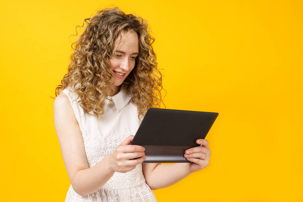 Portret van een jonge vrouw die communiceert op een tablet. Vrouwelijk portret. Geïsoleerd op gele achtergrond - Foto, afbeelding