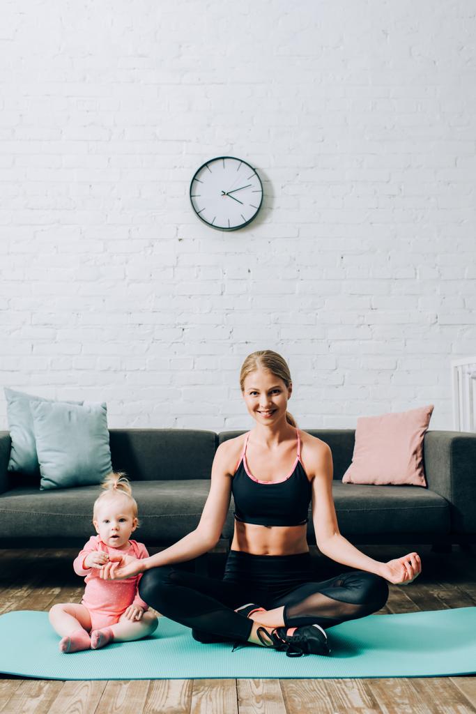 Nainen urheiluvaatteet istuu jooga poseeraa lähellä tytär fitness matto  - Valokuva, kuva