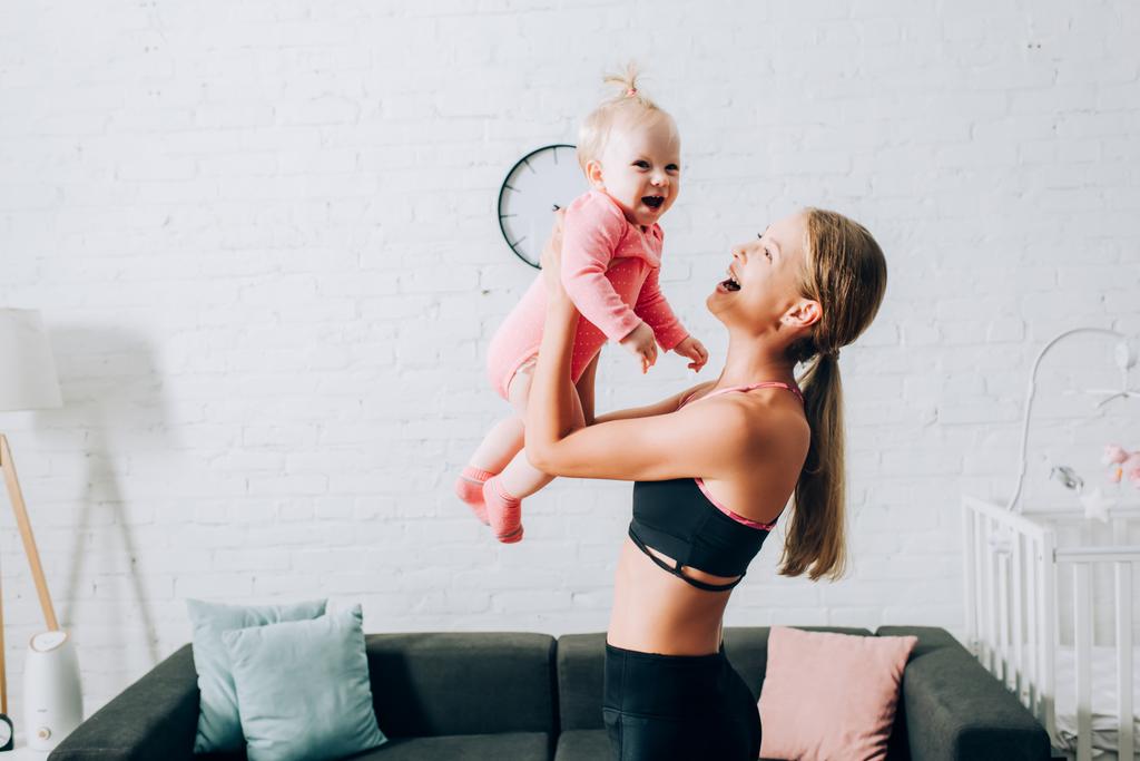 Žena ve sportovním oblečení drží kojeneckou dívku v obývacím pokoji  - Fotografie, Obrázek
