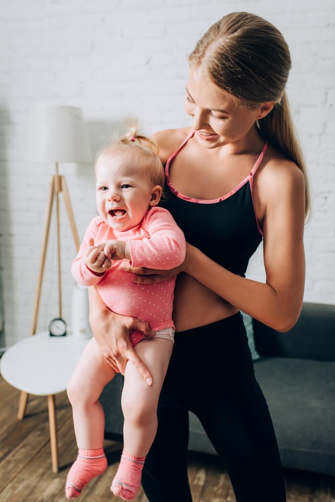 Fit woman holding baby daughter in living room  - Photo, Image