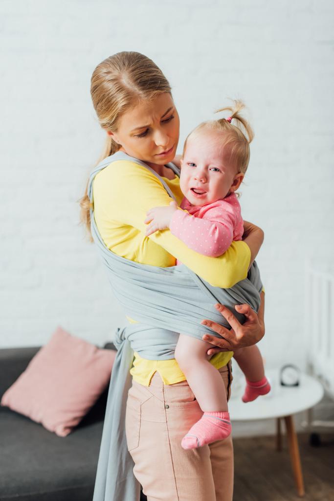Γυναίκα κρατώντας κλάμα κόρη βρέφος στο μωρό σφεντόνα στο σπίτι  - Φωτογραφία, εικόνα