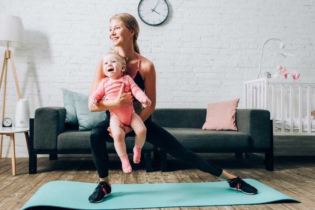 Жінка тренується на фітнес килимі і тримає дочку вдома
  - Фото, зображення