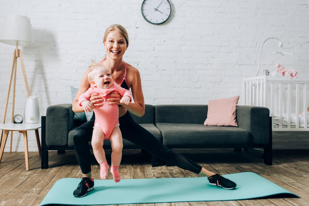 Desportista fazendo lunges no tapete de fitness e carregando bebê filha  - Foto, Imagem