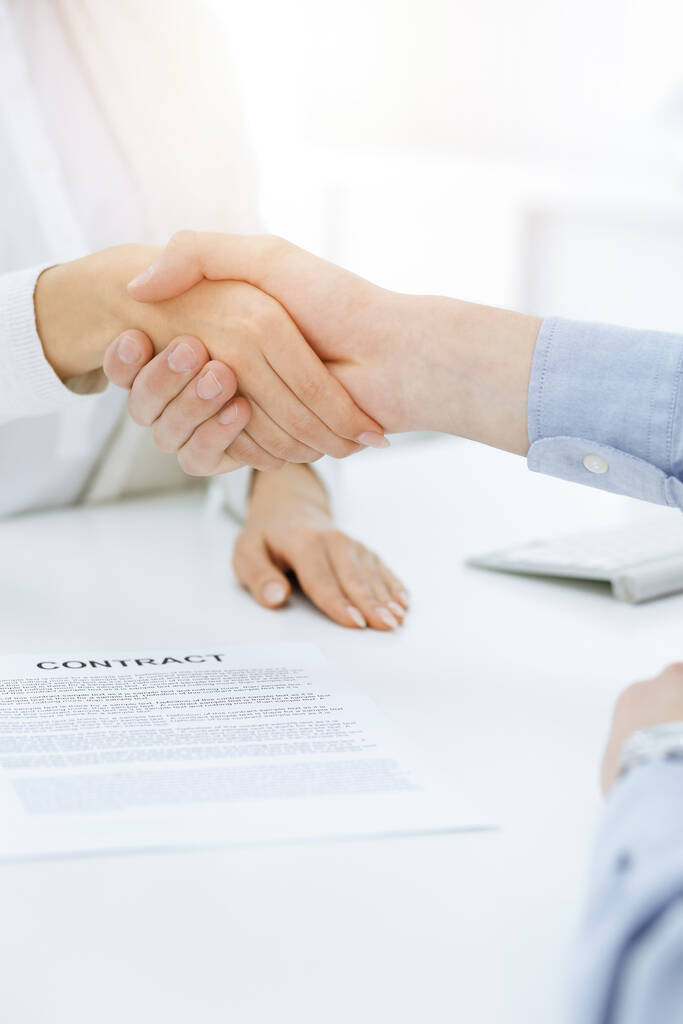 Casual geklede zakenman en vrouw schudden handen na het contract tekenen in het zonnige kantoor. Handdruk concept - Foto, afbeelding