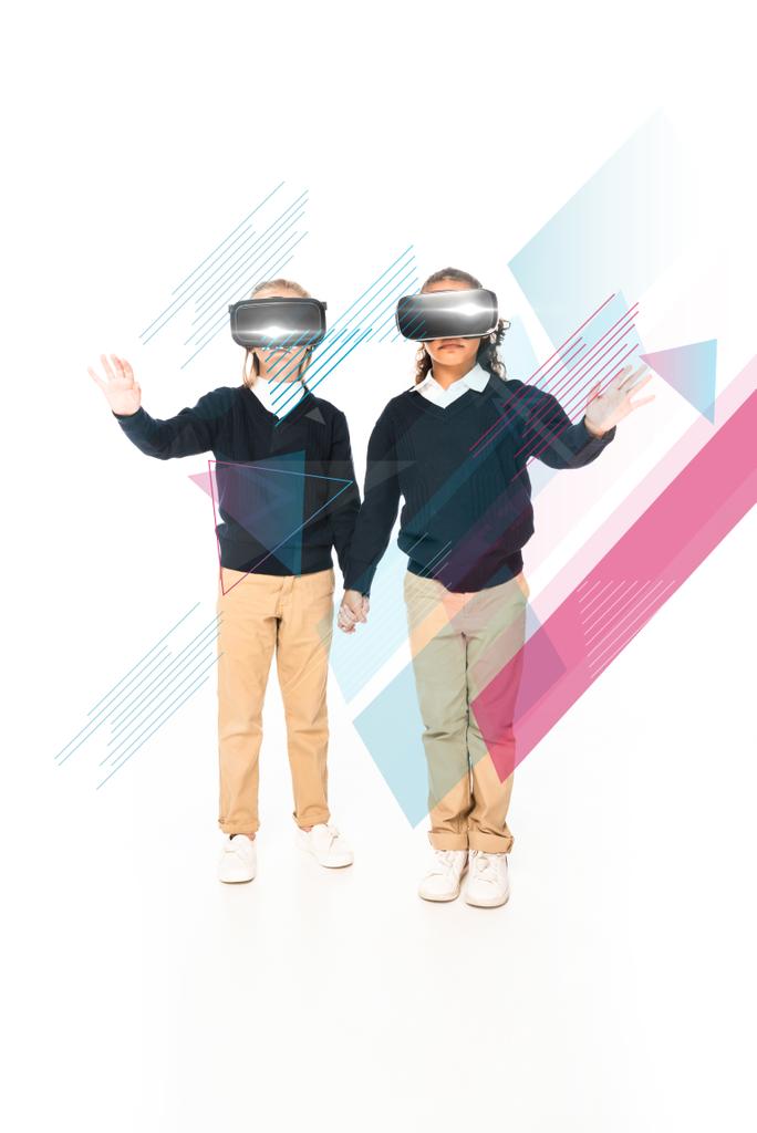 vue complète des écolières multiculturelles tenant la main tout en utilisant des casques de réalité virtuelle sur fond blanc, illustration abstraite - Photo, image
