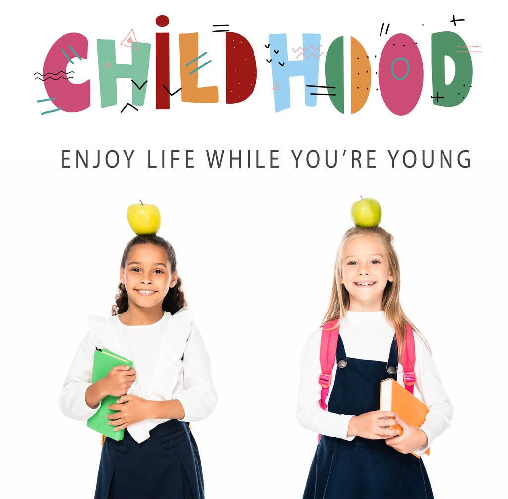 мультикультурні школярки з яблуками на головах тримають книги ізольовані на білому, дитяча ілюстрація
 - Фото, зображення