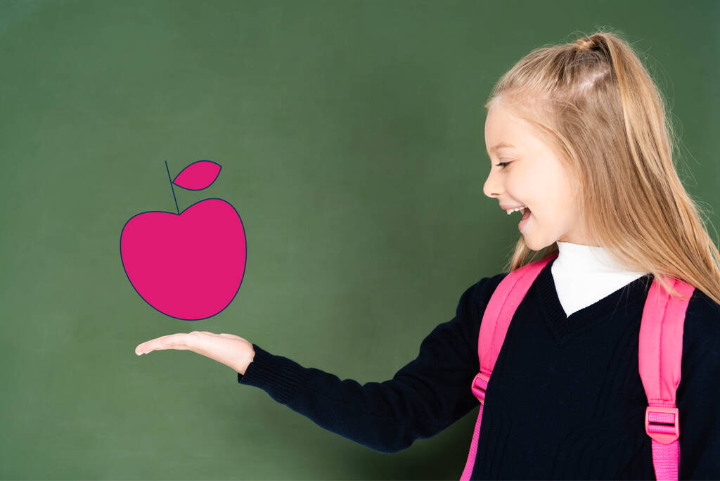 μαθήτρια δείχνει με το χέρι στο εικονογραφημένο ροζ μήλο σε πράσινο πίνακα  - Φωτογραφία, εικόνα