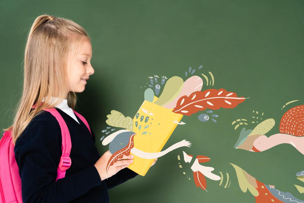Seitenansicht von Schulmädchen Lesebuch mit Fee Illustration in der Nähe grüne Tafel - Foto, Bild