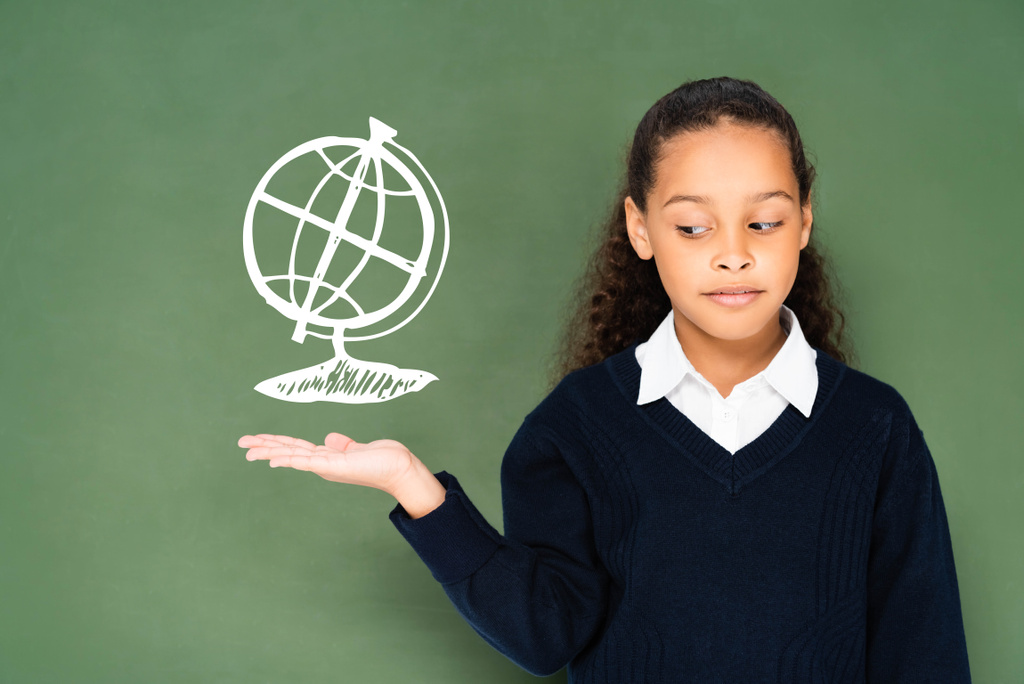 sceptisch schoolmeisje wijzend met de hand naar wereldbol op groen schoolbord  - Foto, afbeelding