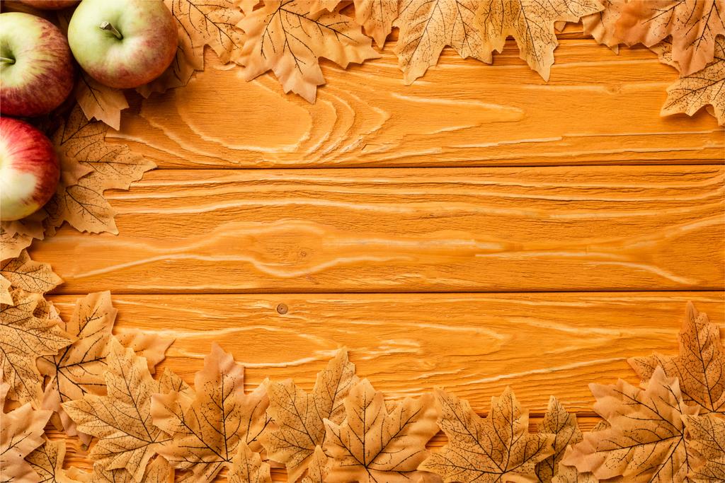 pohled shora na zralá jablka a podzimní zeleň na dřevěném pozadí - Fotografie, Obrázek
