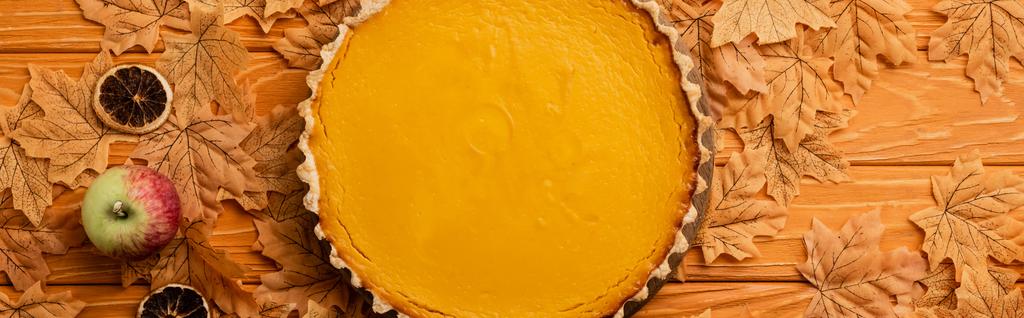 top view of pumpkin pie with apples, dried citrus fruit and autumnal foliage on wooden background, panoramic shot - Photo, Image